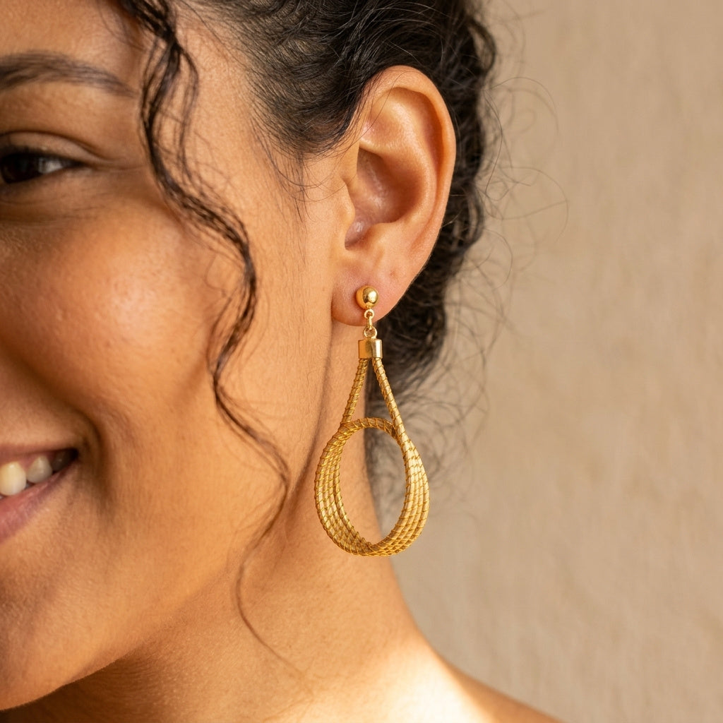 Boucles d'oreilles goutte en capim dourado portées par une femme, vue détaillée à l'oreille, design pendant naturel