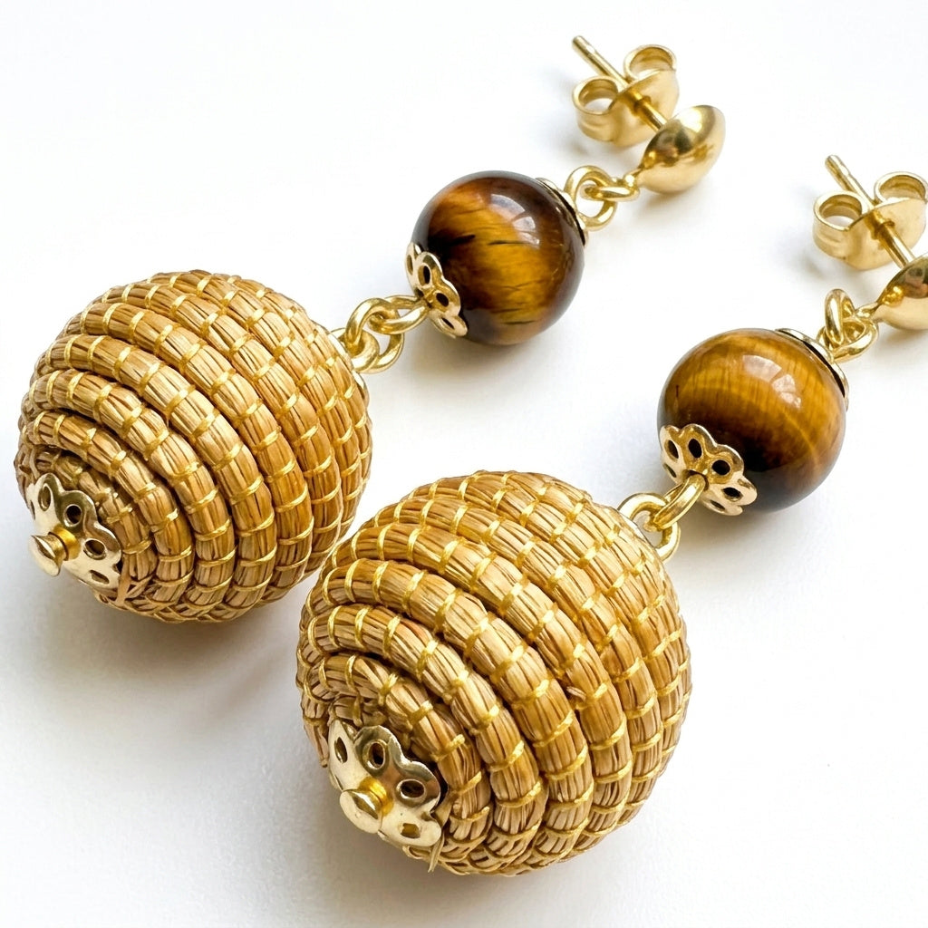 Boucles d'oreilles Jacaré, détail de la sphère tressée en capim dourado et de la pierre naturelle œil de tigre, gros plan