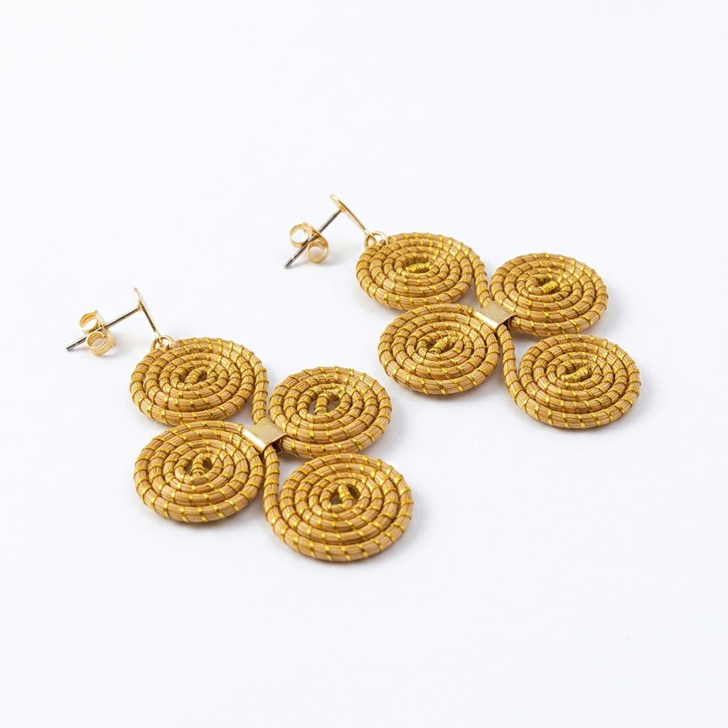 Boucles d'oreilles Cantão, bijou graphique artisanal en herbe dorée, vue trois quarts montrant les quatre spirales en relief