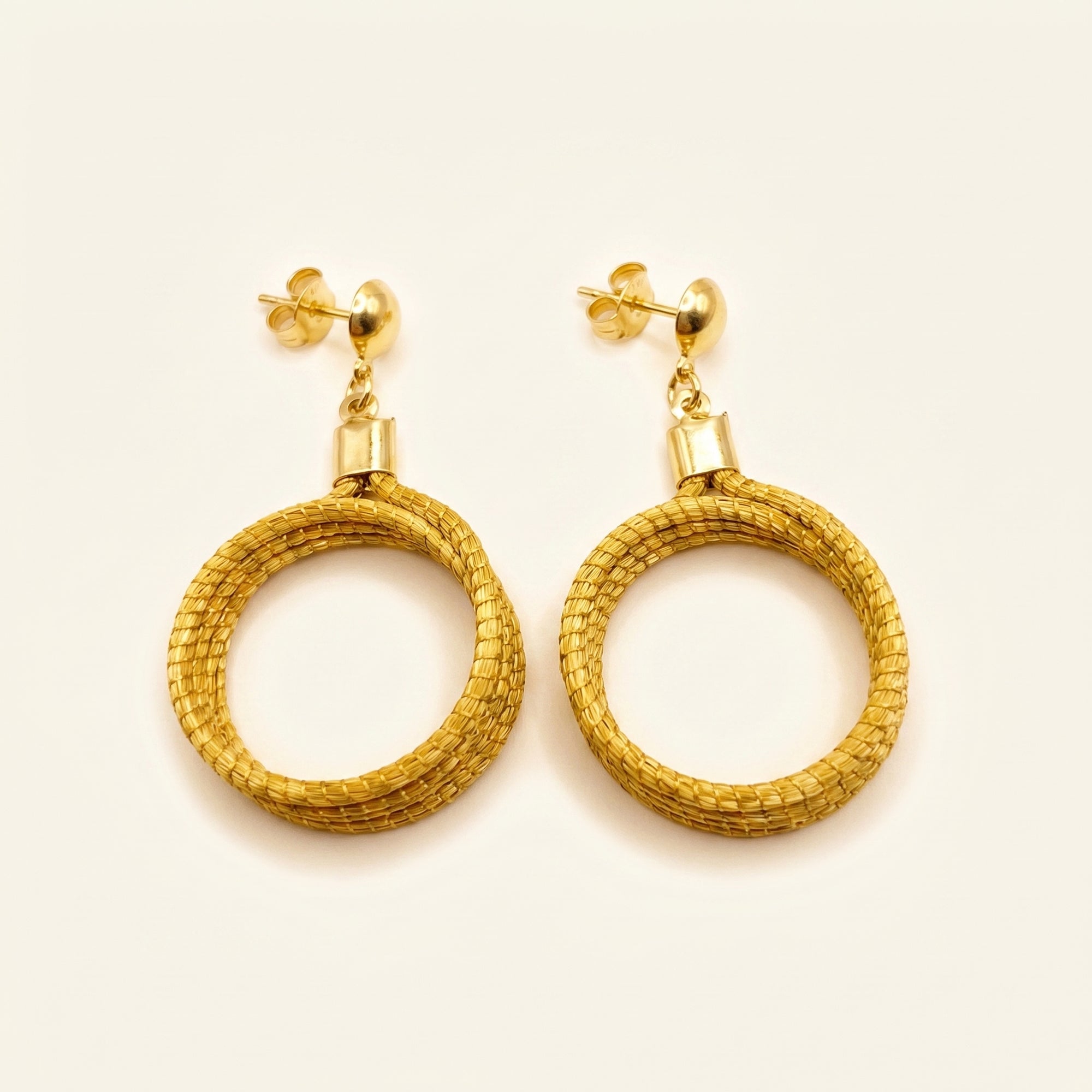 Boucles d'oreilles créoles tressées en capim dourado, fibre dorée du Brésil, vue frontale sur fond clair