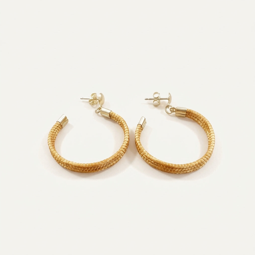 Boucles d'oreilles Embé en capim dourado, créoles ouvertes tressées en fibre dorée du Brésil, vue frontale sur fond clair