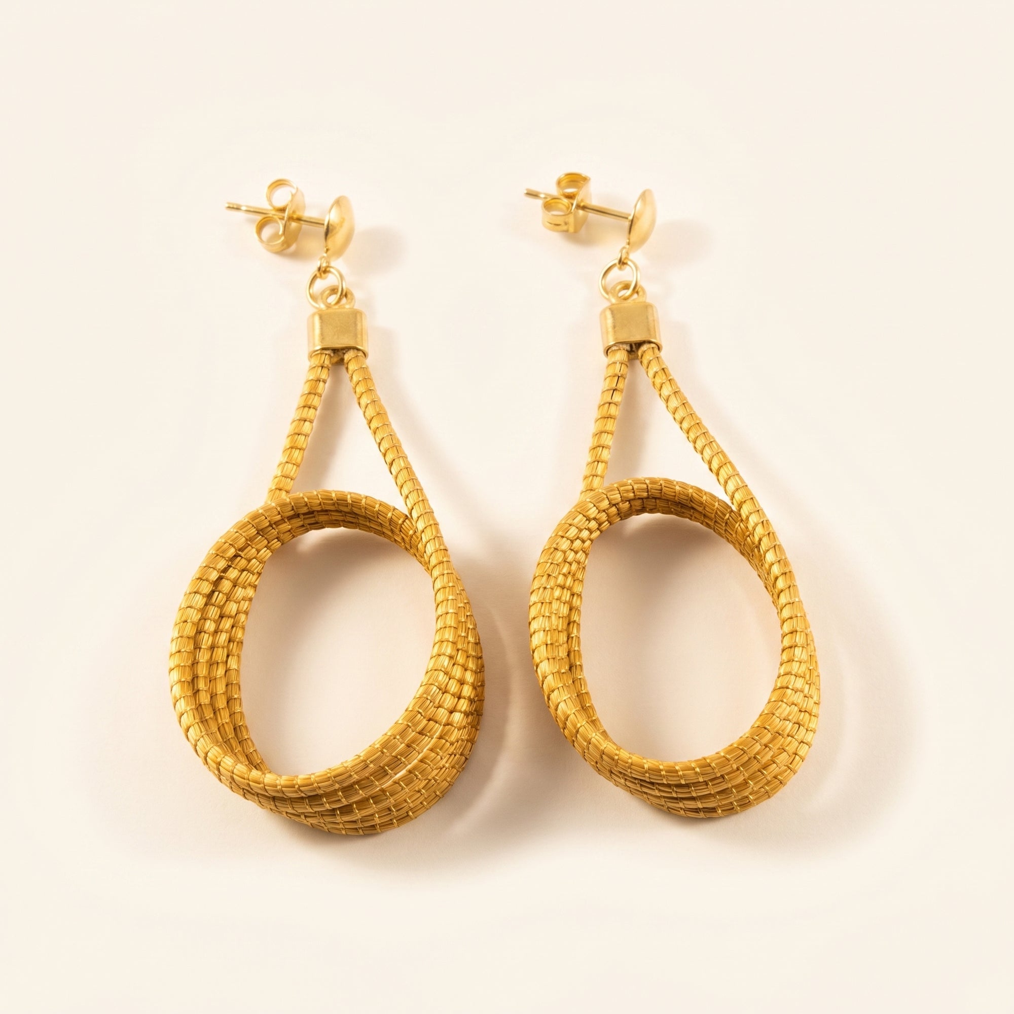 Boucles d'oreilles goutte tressée en capim dourado, fibre dorée du Brésil, vue frontale sur fond clair