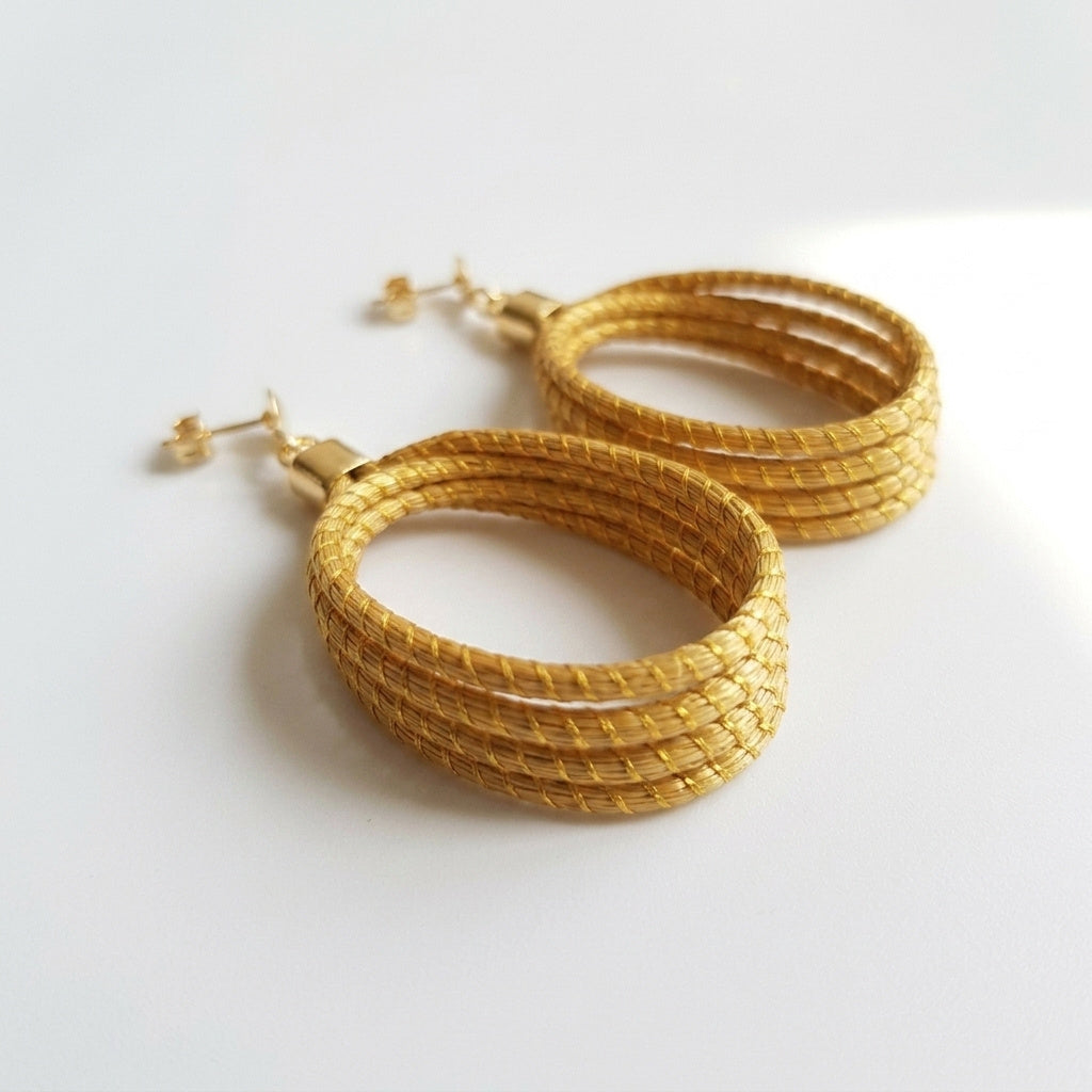 Boucles d'oreilles Guariba, bijou artisanal brésilien torsadé en herbe dorée, vue trois quarts avec ombre