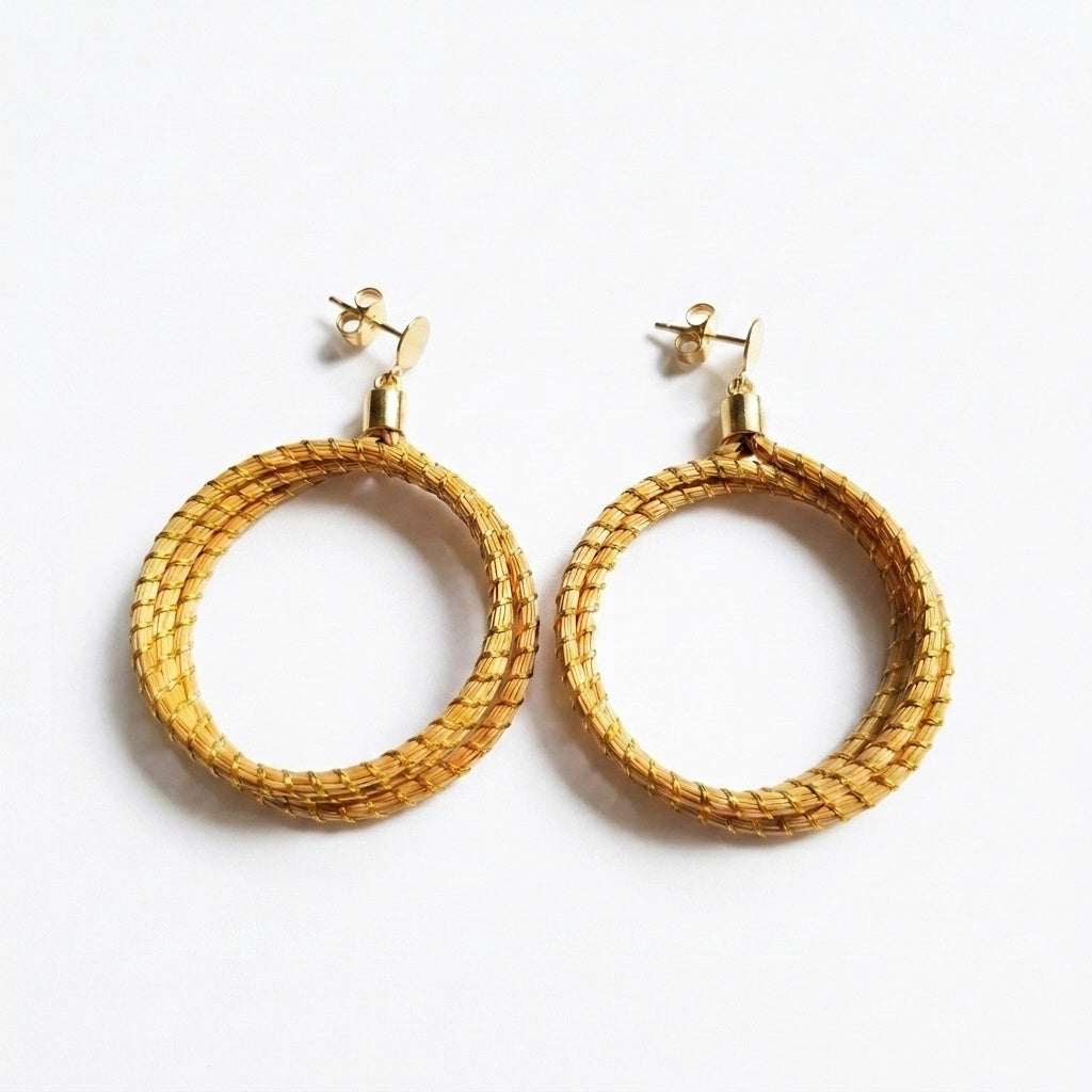 Boucles d'oreilles Icara en capim dourado, double orbite tressée en fibre dorée du Brésil, vue frontale sur fond clair
