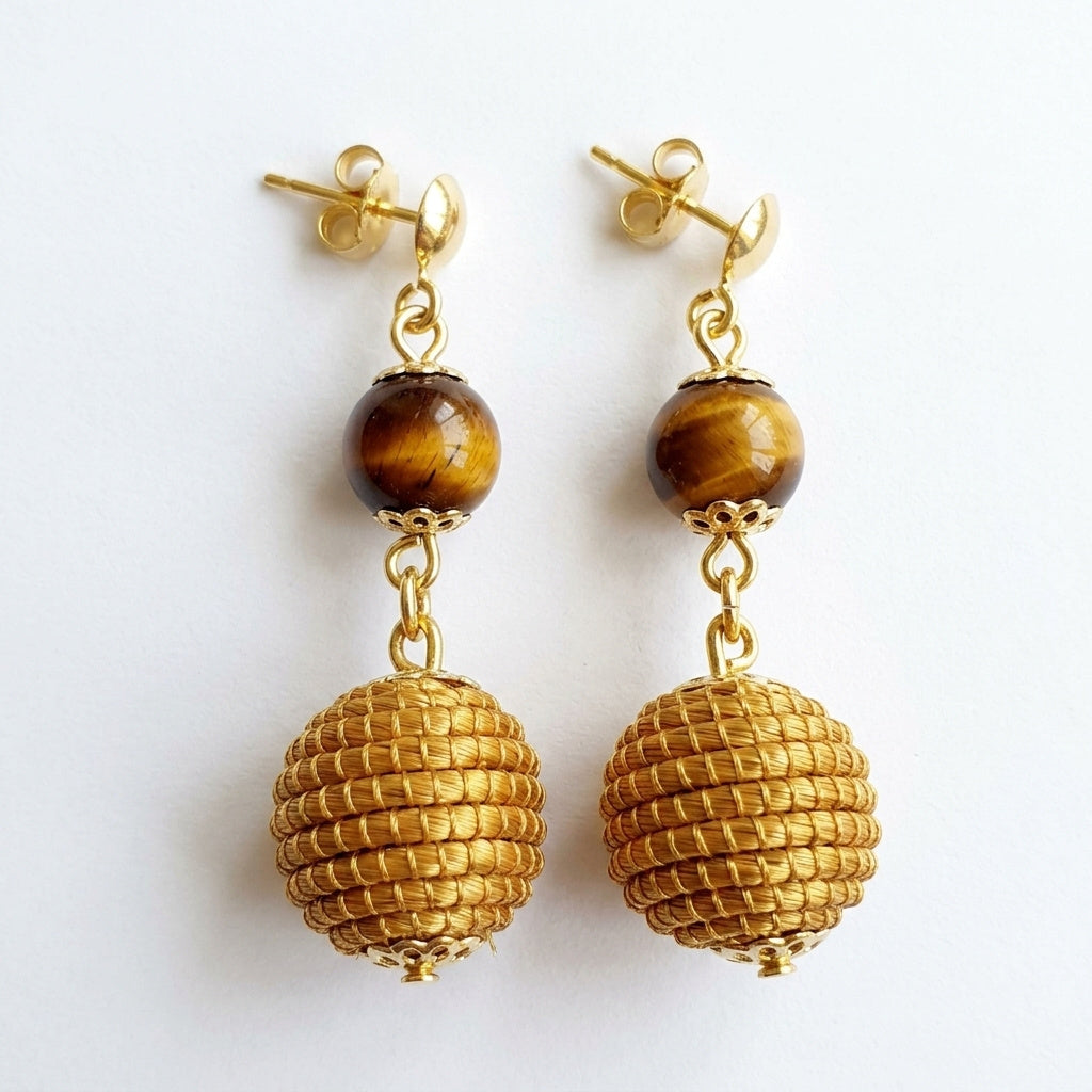 Boucles d'oreilles Jacaré en capim dourado et pierre œil de tigre, sphère tressée en fibre dorée du Brésil, vue frontale sur fond blanc