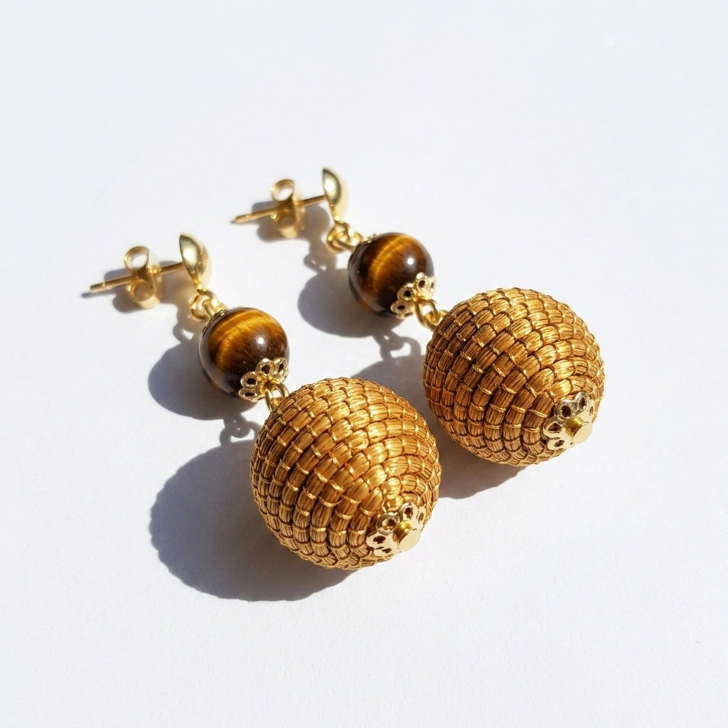 Boucles d'oreilles pendantes Jacaré avec pierre ambrée œil de tigre, sphère tressée en capim dourado, vue trois quarts ombrée