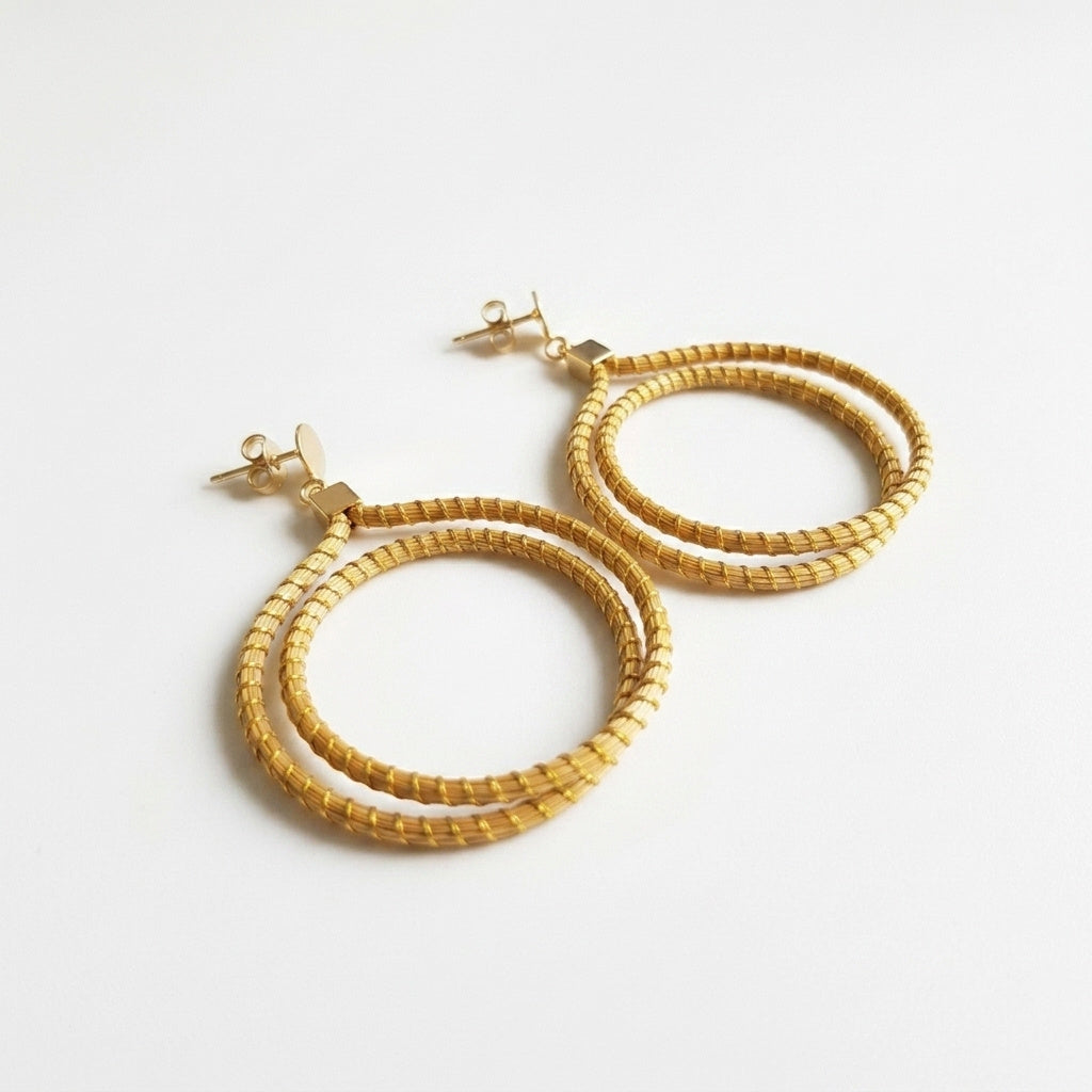 Boucles d'oreilles Jurema en capim dourado, double créole tressée en fibre dorée du Brésil, vue frontale sur fond clair