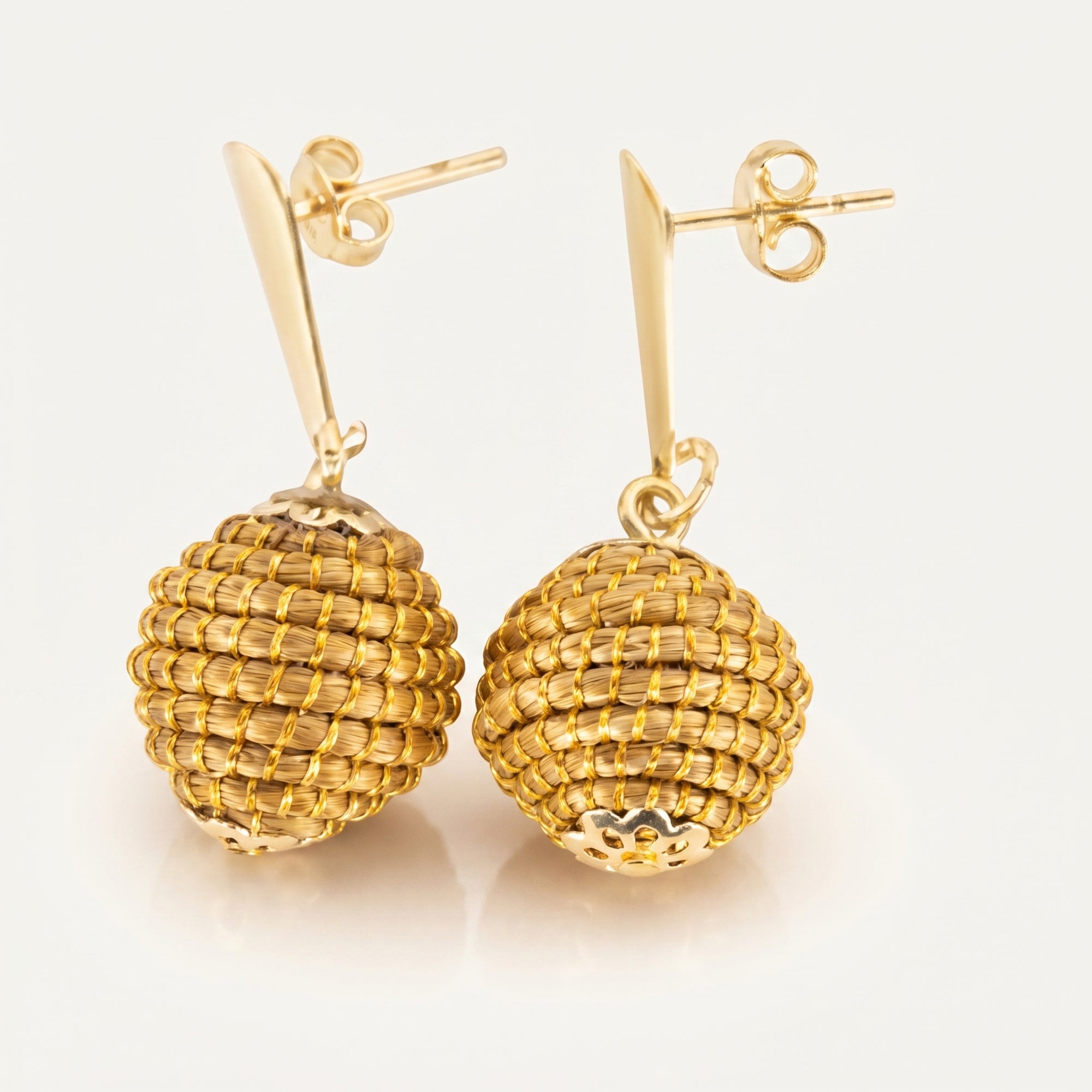 Boucles d'oreilles Poranga en capim dourado, sphère tressée en fibre dorée du Brésil, vue trois quarts sur fond clair