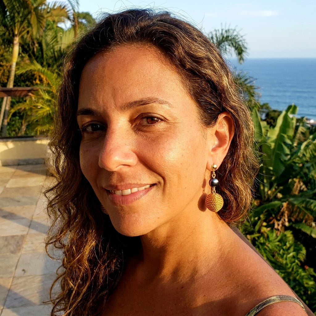 Boucles d'oreilles Taperá en capim dourado et hématite portées par une femme face à l'océan au Brésil, ambiance tropicale