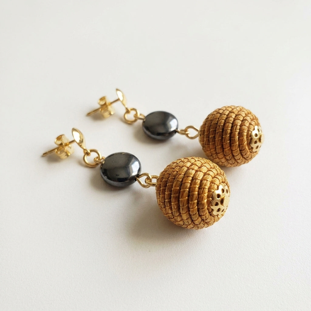 Boucles d'oreilles tressées Taperá avec perle grise, sphère en capim dourado du Jalapão, vue trois quarts à plat