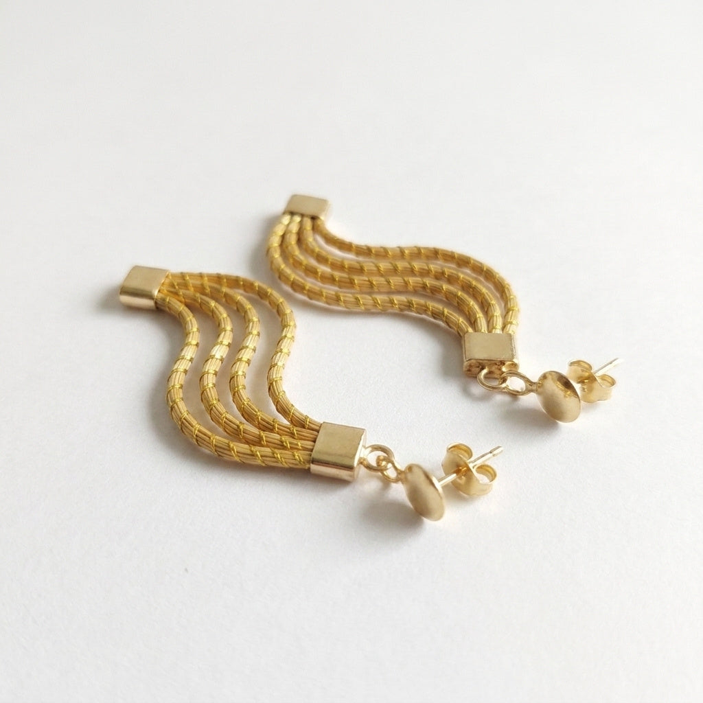Boucles d'oreilles Taua en fibre végétale et or végétal, capim dourado tressé en vagues, vue trois quarts rapprochée
